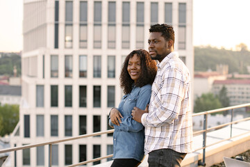 Young African American couple woman and man hugging on rooftop of modern building and looking away....