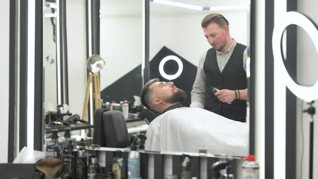 Cutting a gentlemans beard in a barbershop with a clipper. Shortening the length of the beard from the sides by the master for the client.