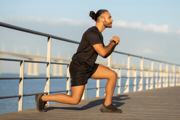 man in sportswear demonstrating a lunge deep exercise by sea