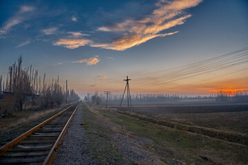 A railroad disappearing into the distance amidst fields in rural scenery, accompanied by old wooden...