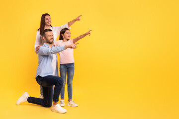family of parents and daughter pointing at empty space, studio