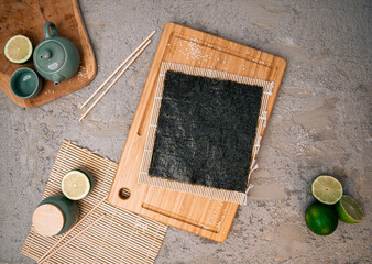 Nori seaweed sheet on wooden cutting board, lime, ceramic green teacup on a modern concrete...
