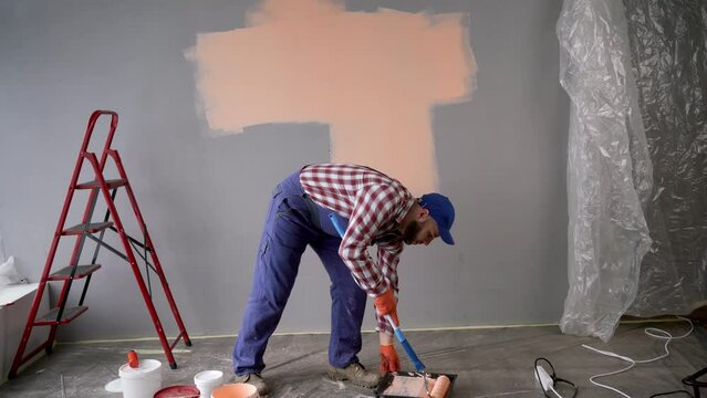 Bearded worker or painter painting walls with a paint roller. Home renovation