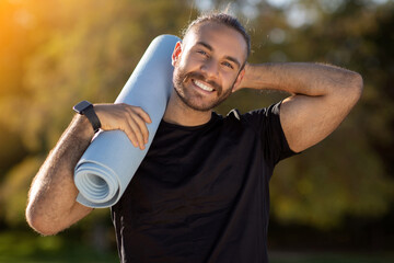 Cheerful and fit European man holding fitness mat stands outdoors