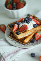 Home made waffles with whipped cream on top and fresh strawberries and blueberries perfect for breakfast close up selective focus