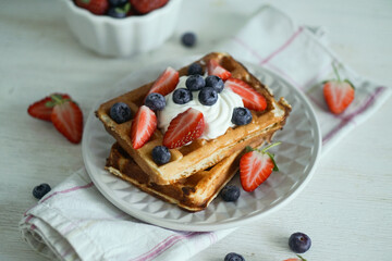 Home made waffles with whipped cream on top and fresh strawberries and blueberries perfect for breakfast close up selective focus