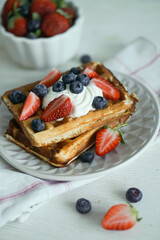 Home made waffles with whipped cream on top and fresh strawberries and blueberries perfect for breakfast close up selective focus