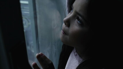 Lonely child feeling sad and depressed in moody winter scene by glass window. One thoughtful little girl stuck at home