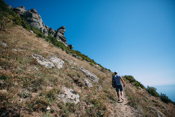 Fototapeta premium A male tourist is climbing up a mountain trail. A man with a backpack is doing mountain hiking. Hiking in the mountains in summer