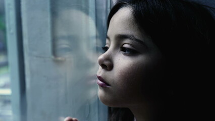 One depressed child leaning on glass window feeling sad and lonely at home, one small introspective...