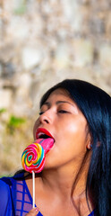 Sexy Latin young woman with bright red sensual lips passionately and sensually licking a colorful spiral lollipop with her beautiful long pink tongue sticking out with her mouth open.