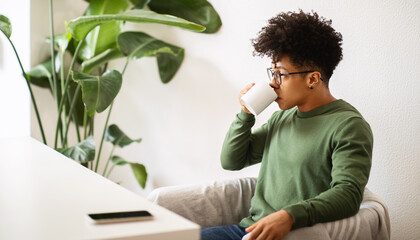 Cool millennial black guy sitting at cafe, drinking coffee