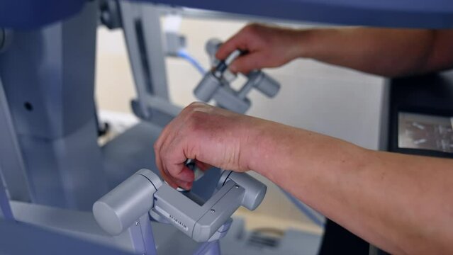 Bare male hands move the manipulators in order to perform the laparoscopic operation with the robotic surgeon. Doctor operates Da Vinci surgeon robot. Close up.