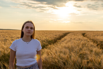 Cute girl walking on wheat field at sunset