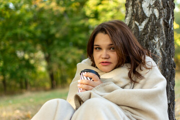 Woman wrapped in a blanket and drinking coffee in the park