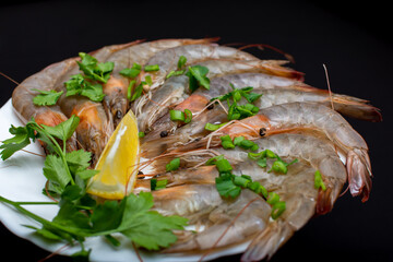 Raw shrimp on a white plate with lemon and herbs