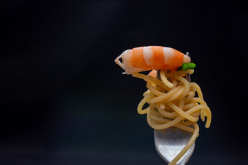 Juicy shrimp with spaghetti on a fork on a dark background