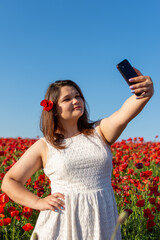 Woman taking selfy against the background of a blooming poppy field