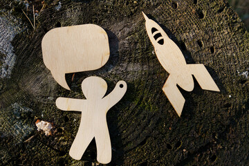 Wooden cutouts of astronaut, speech bubble, and rocket on a tree stump during daytime