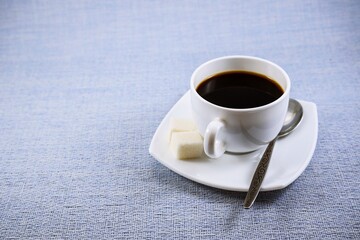 A cup of black coffee with sugar on a beautiful saucer on the table early in the morning