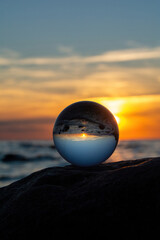 Ball made of glass lies on a stone in which the beach and the sea are reflected