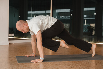 An athletic young man does exercises in the fitness room. A professional guy does yoga in the gym