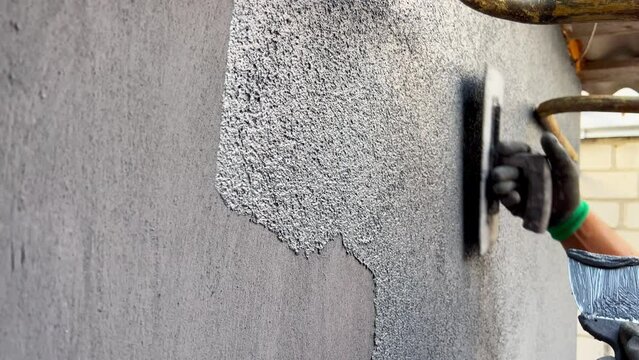 Plastering the external wall with marble chips. Using a spatula, apply decorative marble plaster to the wall. The process of applying a layer of gray plaster. Modern materials for home decoration