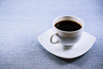 A cup of black coffee on a beautiful saucer on the table early in the morning.