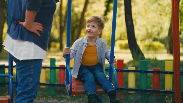 Grandmother pushing swing with grandson in park, leisure activity, recreation