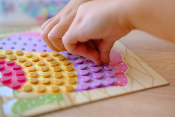 small parts in hands of child, girl plays with mosaic, fill in holes, fine motor skills...
