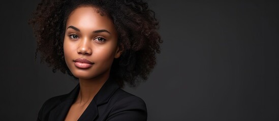 A professional woman with curly hair exudes confidence and strength in a studio setting. She is wearing a black shirt, commanding attention with her presence.