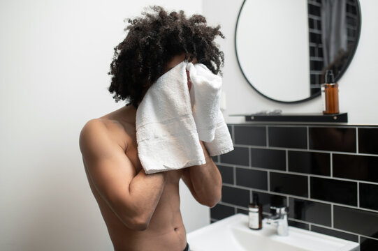 Young man in the bathroom drying off his face with the towel - Powered by Adobe