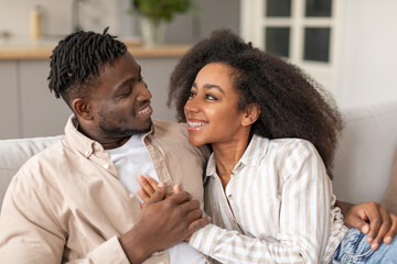 Happy black young couple cuddling sharing embrace in living room