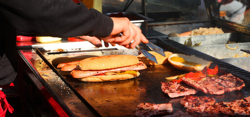 hands of cook at counter of a street food truck preparing sandwiches filled with grilled sausage...