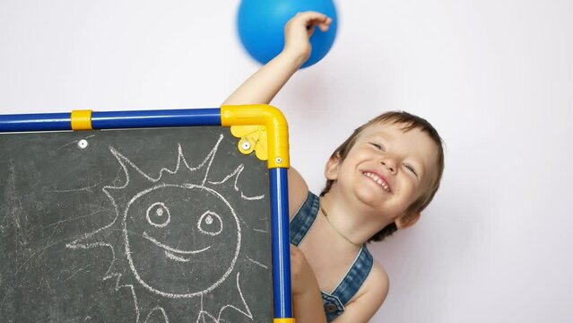 A cute little boy with a blue balloon peeks out from the drawing board and waves a hand greeting