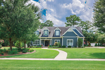 A large blue craftsman new construction house with a landscaped yard and leading pathway sidewalk