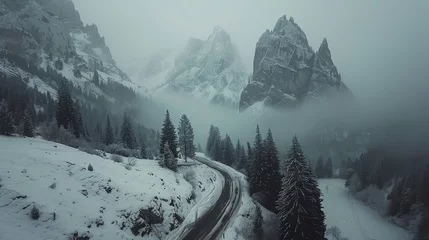 Fototapeten Winter scene with a winding road through a snowy forest and misty mountain peaks. © AdriFerrer