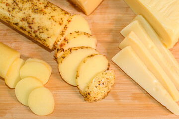 Wooden cutting board with thinly sliced provolone cheese, seasoned provolone cheese, and gruyere cheese slices.