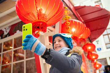 Happy 11 year old European child with a dragon mask on his hat takes a selfie at the Chinese New...