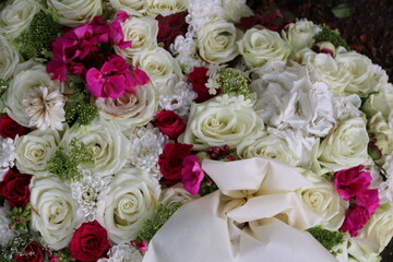 Blumen der Trauer in Weiß und pink mit Schleife im Trauerkranz nach Beerdigung auf dem Friedhof
