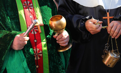 priest with cassock and aspergillum while performing the blessing also with holy water and incense...