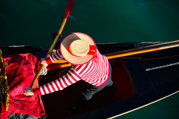 Venetian gondolier with hat and typical white and red dress while rowing on the gondola on the...
