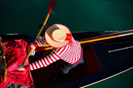 Venetian gondolier with hat and typical white and red dress while rowing on the gondola on the grand canal in Venice Italy