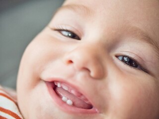 A close-up view capturing the joyful expression of a baby who is smiling and showing two little teeth. The childs eyes sparkle with delight, and theres a hint of playfulness in this candid moment.