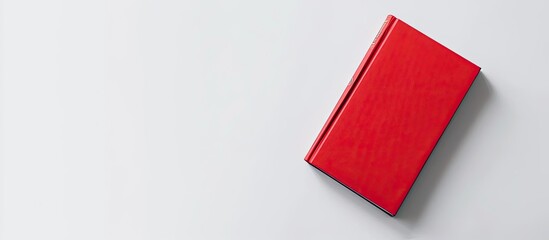 A vibrant red book is positioned on top of a clean, white table surface. The contrast between the bold red color and the pristine white background creates a visually striking display.