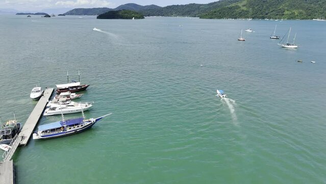 Aerial shot drone follows small speedboat to end of marina before turning left to look back at the port