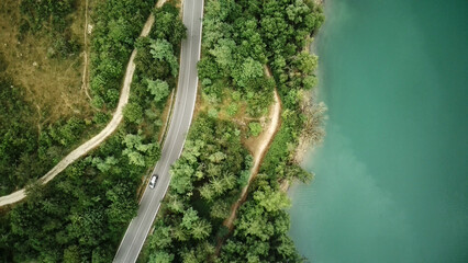 This aerial view shows a winding road cutting through dense forested area. The road twists and...