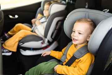 Adorable boy with his sister together in modern car locked with safety belts enjoying family...