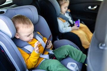 Brother and sister on car back seat holding smart phones while traveling.