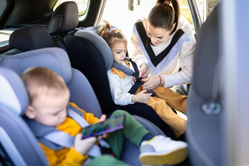 Side view of two children in baby booster car seats and mother fastening seat belts.
